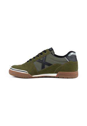 Zapatilla baja verde y negra con suela de goma, cordones negros y detalle reflectante en el talón, mostrada desde el lado exterior.