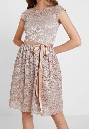 Sleeveless pale pink lace dress with floral pattern, fitted bodice, scalloped hem, and satin ribbon tied in a bow at the waist.
