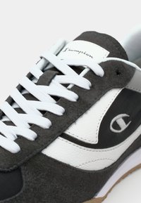 Grå mocka och vit läder sneakers med vita snören, med en logotyp och en texturerad sula. Närbild som framhäver detaljer.