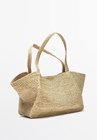 Borsa a tracolla in paglia intrecciata beige con due lunghi manici, apertura ampia e motivo intrecciato testurizzato su sfondo bianco.