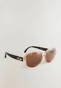 Lunettes de soleil avec une monture surdimensionnée de couleur rose pâle, des verres teintés marron et des branches en écaille de tortue avec un accent métallisé près des charnières.