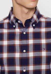 Camicia a quadri blu, marrone e bianca con colletto button-down e logo. Tessuto in cotone con una texture liscia e vestibilità regolare.