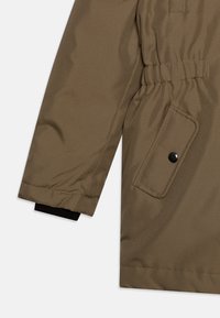 Olivovo zelená prešívaná bunda so zakončeniami rukávov na gumičku, bočná kapsa so čiernym cvokom a zhromaždená látka na zápästí pre lepšie prispôsobenie.