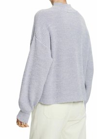 Lichtgrijze gebreide trui met een hoge hals, verlaagde schouders en geribbelde accenten. Gestructureerde stof; losse pasvorm, gecombineerd met lichtgekleurde broek.