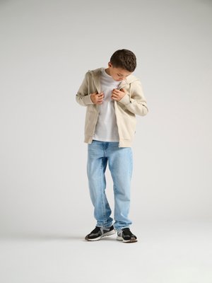 Beige zip-up hoodie over a white t-shirt, light blue jeans, and black sneakers with gray accents. Subtle texture on the hoodie.