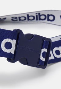 Marinblå justerbar bälte med plastspänne. Har en vävd rem med vit "adidas" text och logotyp. Robust material och mjuk textur.