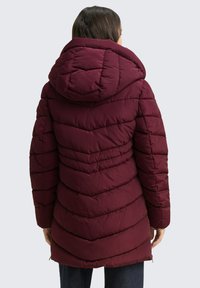 Bordeaux pufferjack met een capuchon, met een geborduurd patroon en een middellange snit. Gladde textuur en een ritssluiting aan de onderkant.