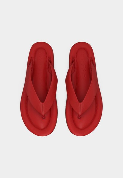 Para czerwonych klapek na lato z grubymi paskami, widziana z góry na jednolitym jasnym tle.