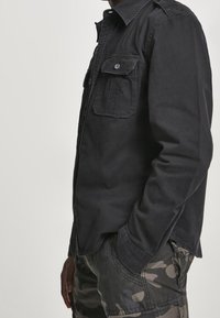 Svart skjorta med knappar, två bröstfickor, lång ärm och regular fit. Tyget har en mjuk, matt yta.