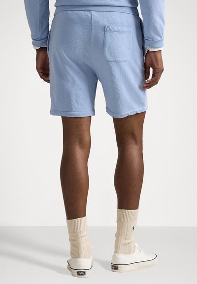 Pantaloni scurti din bumbac de culoare albastru deschis, cu un buzunar la spate, manșete tivite și o croială relaxată, asortați cu pantofi albi și ciorapi crem.