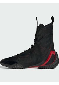 High-top black athletic shoe with textured fabric upper, black laces, and red rubber accent on the heel and sole, featuring a unique shape.