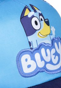 Gorra azul con una corona de tela azul, visera azul marino, que presenta un perro de dibujos animados bordado y el texto "BLUEY" en blanco.