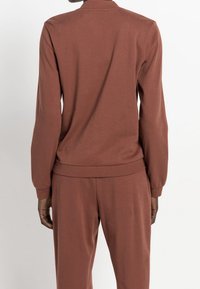 Brun långärmad topp med ribbade muddar och nederkant, tillverkad av mjukt tyg, stylad med matchande byxor, synliga sömdetaljer.