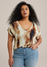 Halenka s výstřihem do V a krátkým rukávem v světle béžové barvě s hnědými a černými tie-dye vzory. Měkká textura a volný střih, součástí jsou světle modré džíny.
