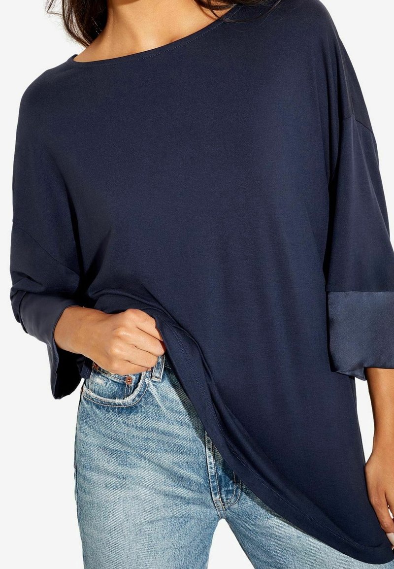 Marinblå oversized topp med bred halsringning och trekvartslång ärm, tillverkad av mjukt tyg. Matchad med ljusblå denimjeans.