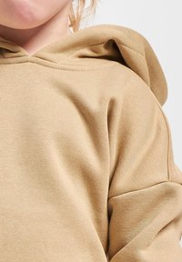 Sudadera con capucha de color caqui, con tejido texturizado, costuras prominentes y un corte holgado. La capucha tiene contornos suaves, lo que realza el diseño casual.