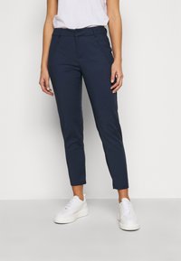 Pantaloni blu navy su misura con vestibilità slim, dotati di tasche laterali e passanti per cintura, abbinati a sneaker platform bianche.