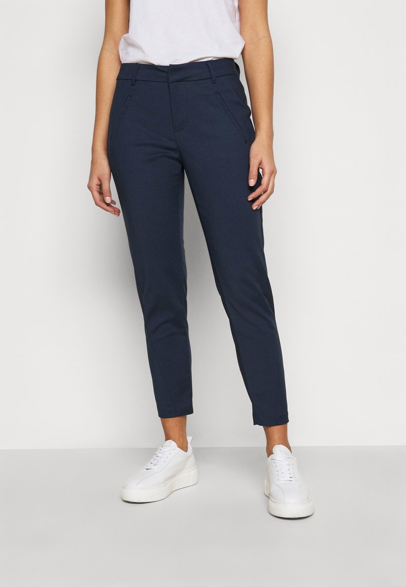 Pantaloni blu navy su misura con vestibilità slim, dotati di tasche laterali e passanti per cintura, abbinati a sneaker platform bianche.