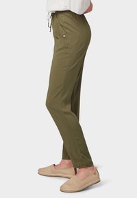 Pantaloni verde oliva con vita con cordoncino, vestibilità slim e dettagli delle tasche laterali. Abbinati a scarpe slip-on beige chiaro.