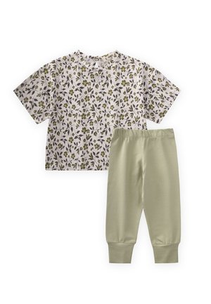 Weißes kurzärmeliges Oberteil mit grünem und grauem Blumenmuster, kombiniert mit hellgrünen Hose mit elastischem Bund und hochgekrempelten Knöcheln.