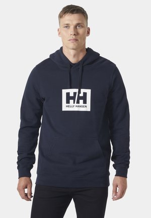 Navy blauwe hoodie gemaakt van katoen. Heeft een wit rechthoekig logo met de tekst "HH" en "HELLY HANSEN". Inclusief een kangoeroezak en een capuchon met trekkoord.