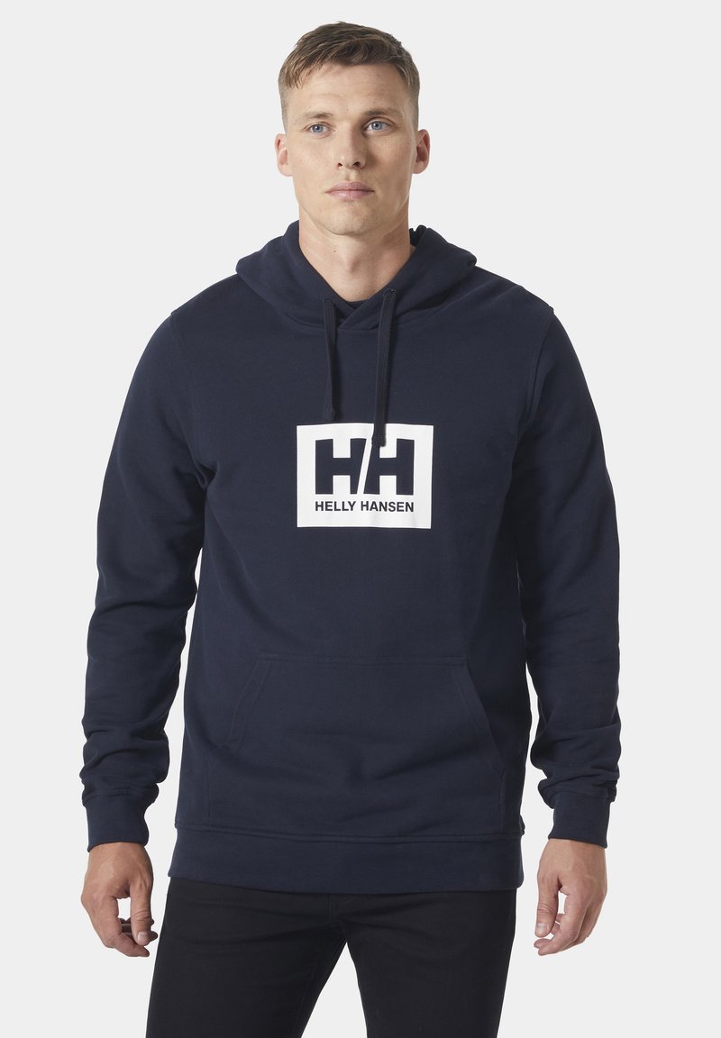 Sudadera de color azul marino hecha de algodón. Presenta un logo rectangular blanco con el texto "HH" y "HELLY HANSEN". Incluye un bolsillo tipo canguro y capucha con cordón.