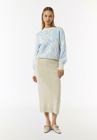 Hellblauer, gemusterter Pullover mit cremefarbigem Rock und beigen Schuhen. Der Pullover hat ein gewelltes Design; der Rock ist knielang und hat eine glatte Textur.