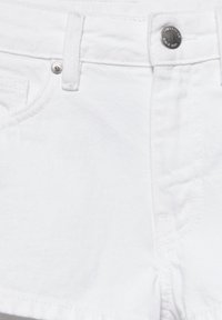 Partie avant d'un jean en denim blanc montrant le bouton, les passants de ceinture et les détails de couture de la poche.