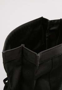 Bolsa de tela negra con forma estructurada, con un forro interno suave y bordes superiores reforzados. Sin herrajes ni adornos visibles.