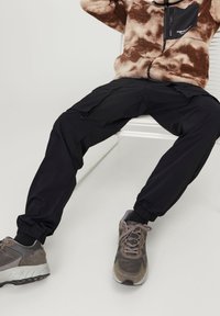 Svarta cargobyxor med elastiska muddar, med sidofickor och en jämn textur. Grå sneakers med en blandning av mocka och meshdetaljer.