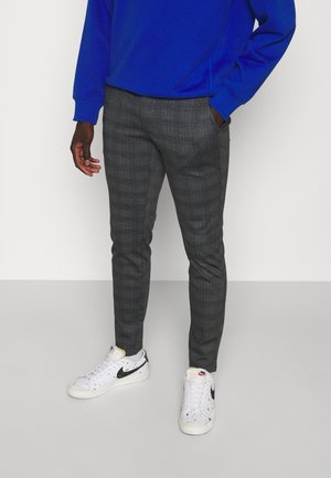 Pantaloni grigi a scacchi con un taglio slim, abbinati a una felpa blu e sneakers bianche con accenti neri e dettagli maculati.
