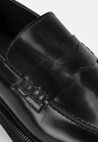Schwarze Lederloafer mit einem Slip-On-Design, glatter Textur, dekorativer Naht und einem erhöhten Band entlang der Oberseite.
