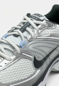 Zapatilla de correr Nike con parte superior de malla en gris y blanco, acentos en plata, logo Swoosh negro, collar acolchado y detalles de cordones en azul claro.