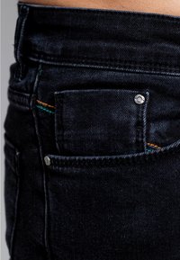 Musta denimmekko, jossa on pieni etutasku, hopeiset metalliosat sekä värikkäät tikkauskoristeet oranssissa ja vihreässä. Sileä tekstuuri.