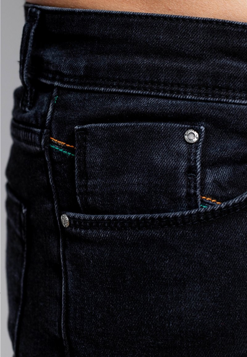 Musta denimmekko, jossa on pieni etutasku, hopeiset metalliosat sekä värikkäät tikkauskoristeet oranssissa ja vihreässä. Sileä tekstuuri.