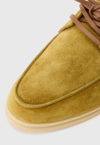 Kollased seemisnahast kingad, millel on sile tekstuur, ümar nina ja heledat värvi kummist tallad. Omavad pruune paelu ja õmblustega ääristatud detaile.