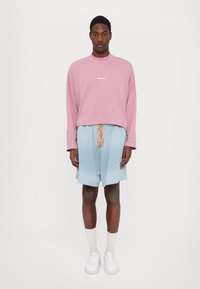 Gaišu rozā garām piedurknēm krekls ar uzrakstu "BONSAI", kombinēts ar gaiši zilām šortiem ar dekoratīvu jostasvietu. Baltas čības un zeķes.