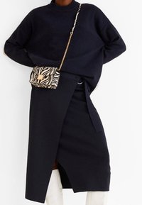 Granatowy sweter dzianinowy z wysokim kołnierzem, zestawiony z spódnicą o kroju kopertowym oraz małą torebką na ramię w zebrzy wzór z złotym zapięciem.