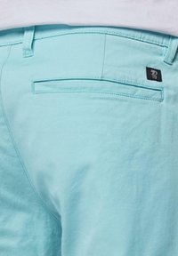Pantaloni azzurri chiari realizzati in tessuto morbido, dotati di una tasca posteriore con apertura orizzontale e una piccola etichetta nera del marchio.