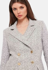 Blazer doppiopetto in motivo houndstooth grigio. Tessuto testurizzato con bottoni in tonalità oro e rever a punta.