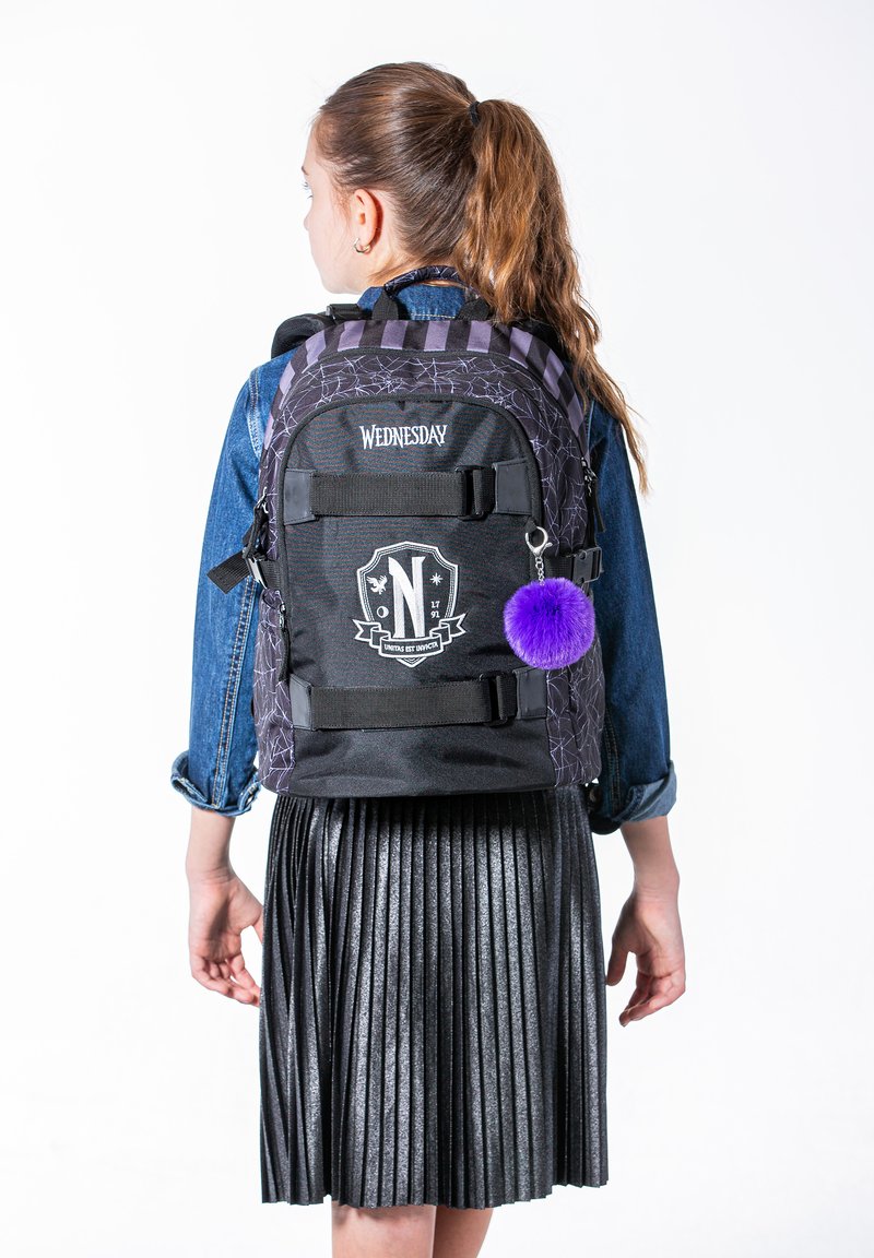 Černý batoh s fialovými detaily, páskem s kostkovaným vzorem a logem, s vnějšími kapsami a fialovým pom-pom přívěskem na klíče.