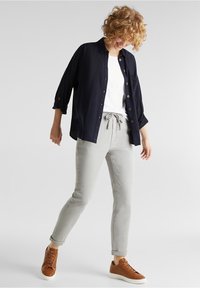 Granatowa koszula zapinana na guziki noszona na białej koszulce, jasnoszare zwężane spodnie, brązowe trampki, luźny krój i podwinięte rękawy.