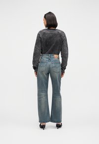 Čierna košeľa s dlhým rukávom v kombinácii s vyblednutými modrými širokými džínsami, ktoré majú svetlý praný vzhľad a klasické zadné vrecká. Viditeľné čierne topánky na vysokom opätku.