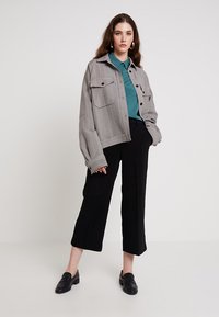 Szürke houndstooth mintás dzseki, két elülső zsebbel, akárcsak egy teal színű inggel és fekete, bő szárú nadrággal párosítva. Fekete loaferek teszik teljessé az öltözéket.