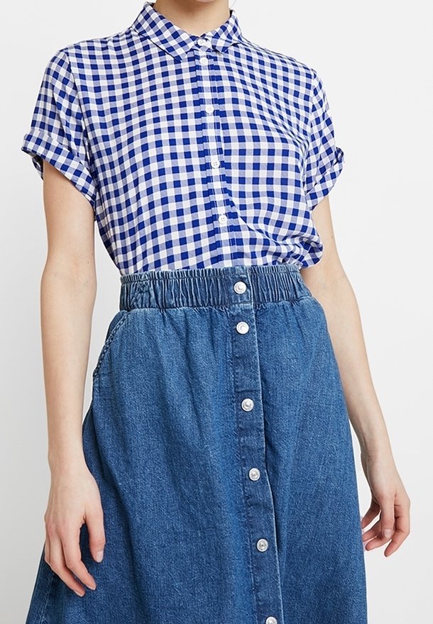 Chemise à manches courtes bleu et blanche à carreaux avec un devant à boutons, associée à une jupe en denim longueur cheville avec une taille froncée et des détails en boutons.
