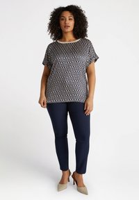Top stampato a maniche corte di colore blu navy con motivo geometrico crema. Abbinato a pantaloni blu navy e scarpe con punta beige. Tessuto morbido.