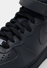 Tamne kožne visokoprihvatljive tenisice s crnim vezicama, podstavljenim okovratnikom i srebrnim detaljima. Sadrže ušivene detalje i ikonični logo swoosh.