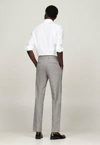 Camicia bianca con colletto, pantaloni grigi su misura con un motivo sottile, e scarpe nere, visti da dietro, enfatizzando la vestibilità e i dettagli di design.