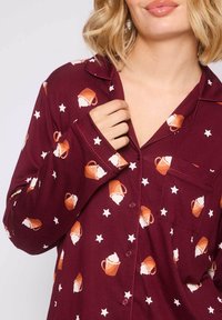 Camisa de pijama color burdeos con diseño de botones, que presenta un patrón de tazas y estrellas en naranja y blanco. Bolsillo notable en el lado izquierdo.