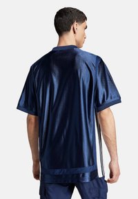 Mörkblå kortärmad tröja i glänsande tyg, med kontrasterande ränder längs sidorna och rundad halsringning.